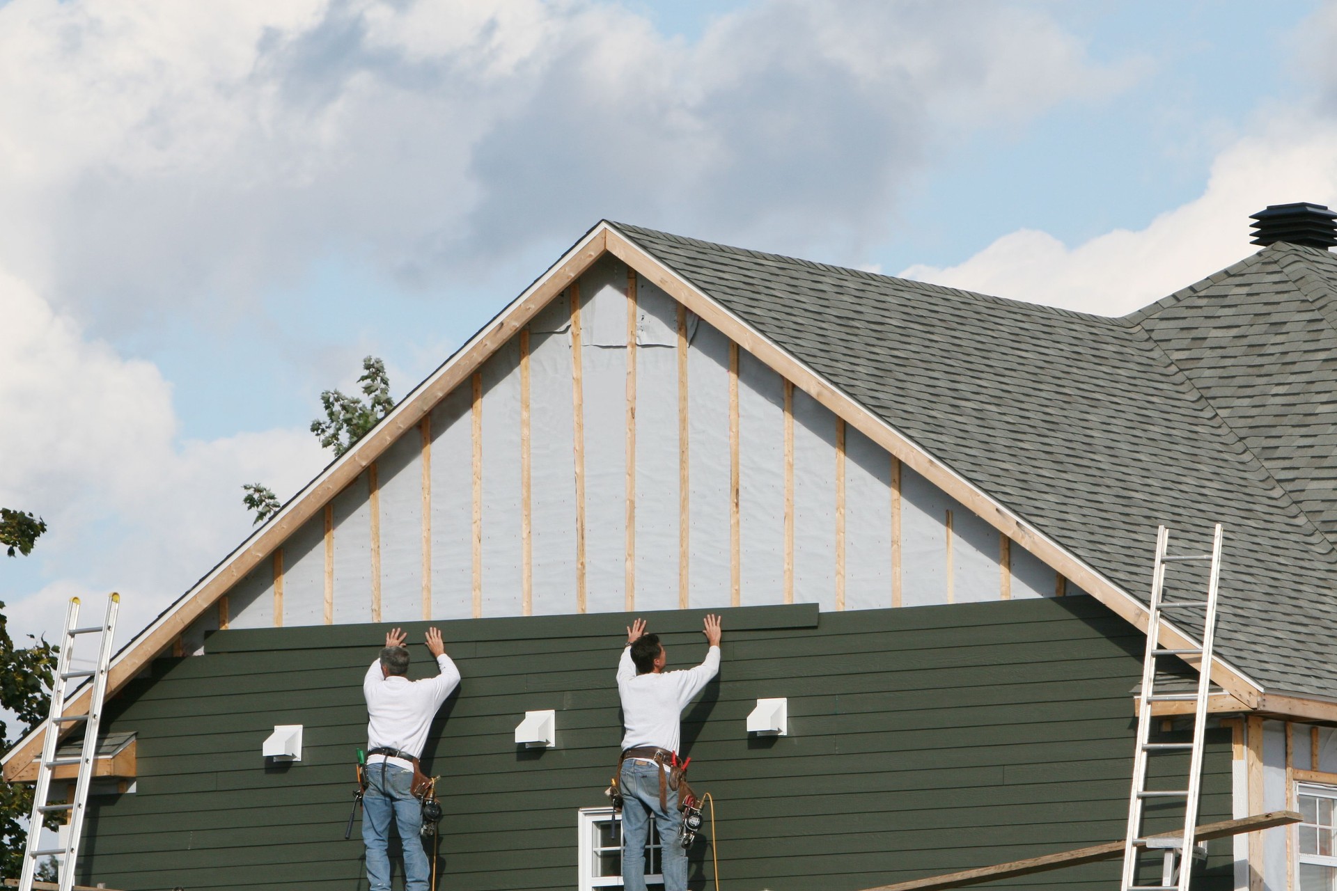 Two men applying green paneling to a house